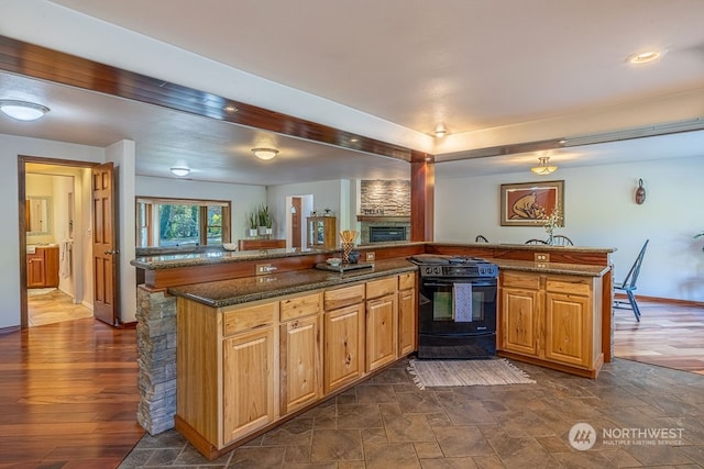 kitchen featuring black stove, a stone fireplace, dark stone counters, and dark hardwood / wood-style flooring