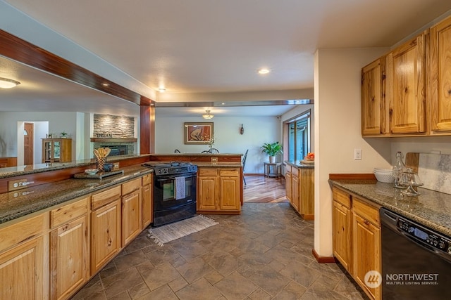 kitchen with dark tile flooring, a fireplace, dark stone countertops, and black appliances