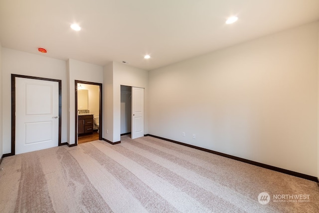 unfurnished bedroom with ensuite bathroom, a closet, and light colored carpet