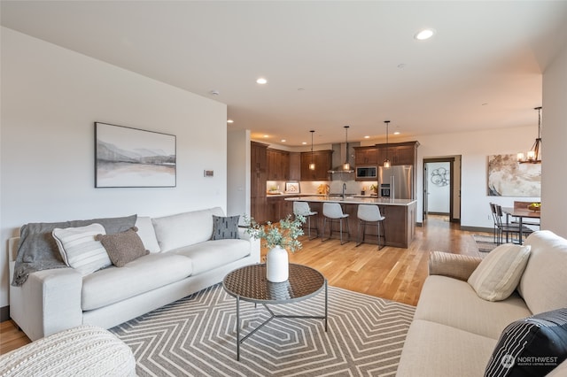 living room with sink, light wood-type flooring, and an inviting chandelier