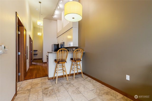 kitchen with light hardwood / wood-style floors, decorative light fixtures, a breakfast bar, white cabinetry, and track lighting