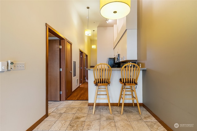 kitchen with pendant lighting, light tile flooring, a towering ceiling, a breakfast bar area, and white cabinets