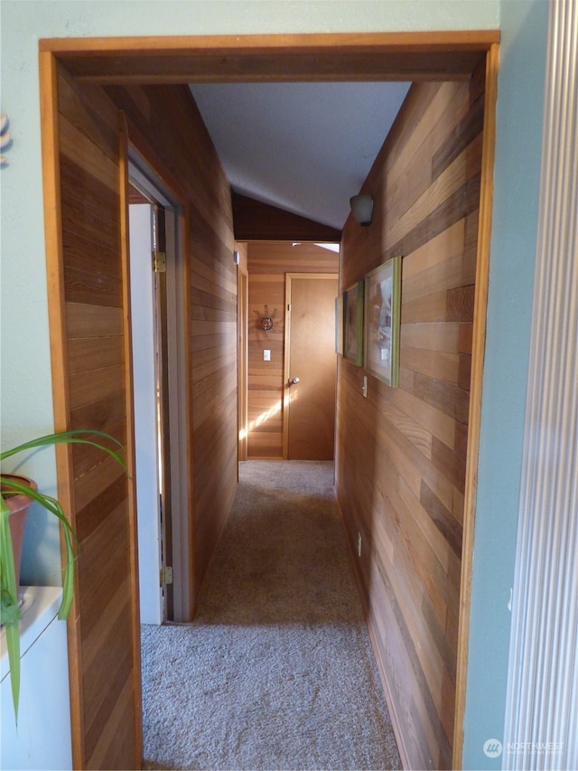 corridor with carpet, wooden walls, and vaulted ceiling