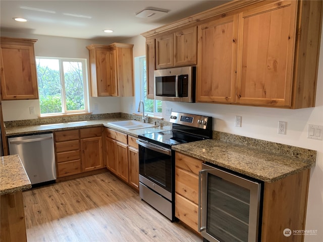 kitchen with appliances with stainless steel finishes, light hardwood / wood-style floors, wine cooler, light stone countertops, and sink