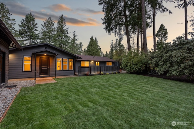 back house at dusk with a deck and a lawn