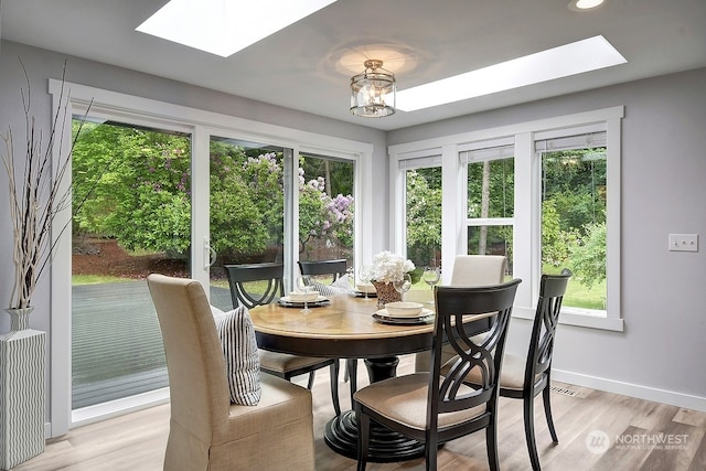 dining room with a skylight, a chandelier, and light wood-type flooring