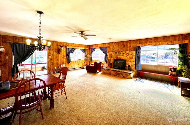 dining room with ceiling fan with notable chandelier, a fireplace, a baseboard heating unit, wood walls, and carpet