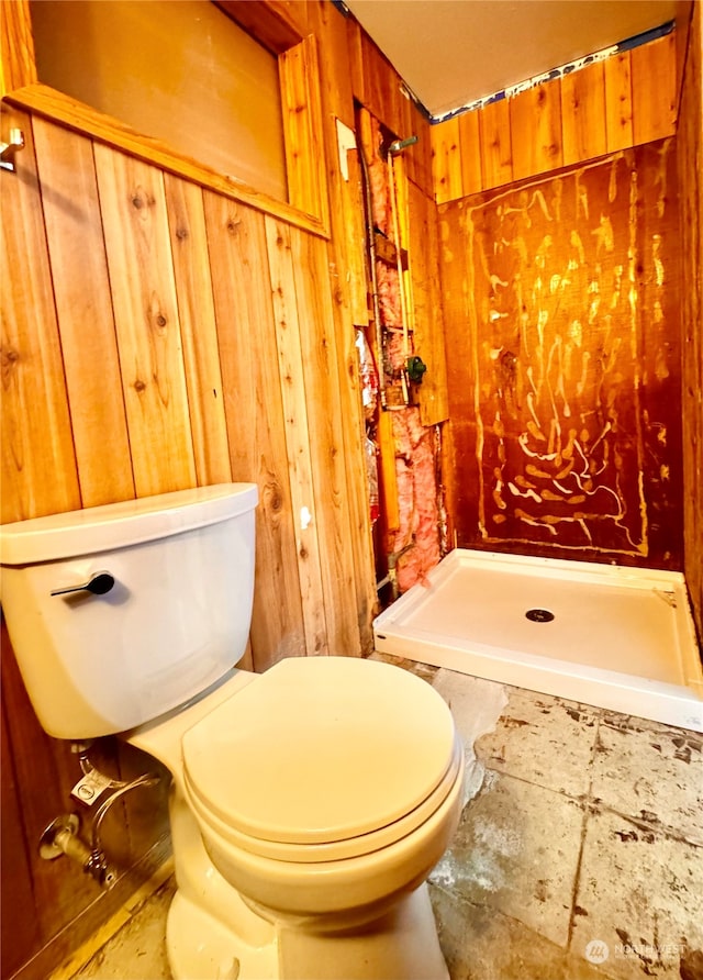 bathroom with wooden walls, tile flooring, toilet, and walk in shower