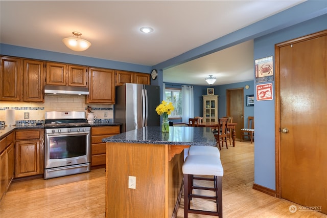 kitchen featuring dark stone counters, a kitchen island, a breakfast bar, light hardwood / wood-style floors, and stainless steel appliances