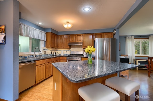 kitchen featuring dark stone counters, a breakfast bar, light hardwood / wood-style flooring, appliances with stainless steel finishes, and sink