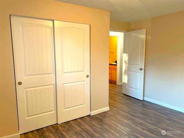 unfurnished bedroom with a textured ceiling, dark wood-type flooring, and a closet