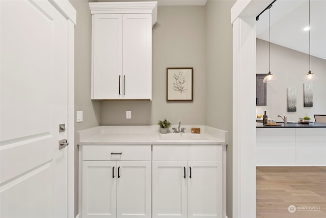 bar featuring sink, light stone counters, white cabinets, decorative light fixtures, and light wood-type flooring