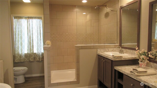 bathroom featuring toilet, vanity with extensive cabinet space, a tile shower, and wood-type flooring