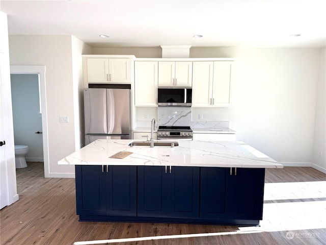 kitchen with light stone countertops, an island with sink, stainless steel appliances, and sink