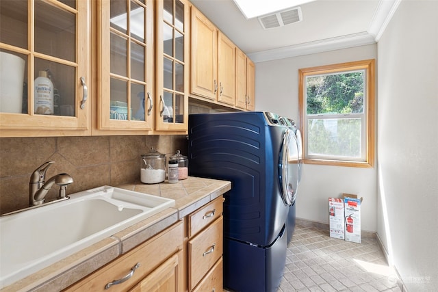 clothes washing area featuring cabinets, sink, light tile flooring, washing machine and dryer, and ornamental molding