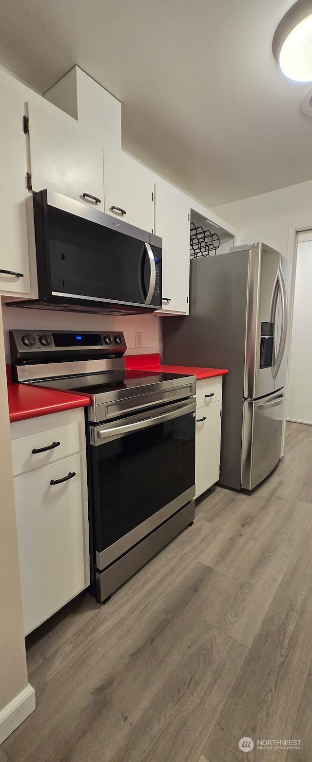 kitchen with appliances with stainless steel finishes, white cabinets, and light hardwood / wood-style flooring