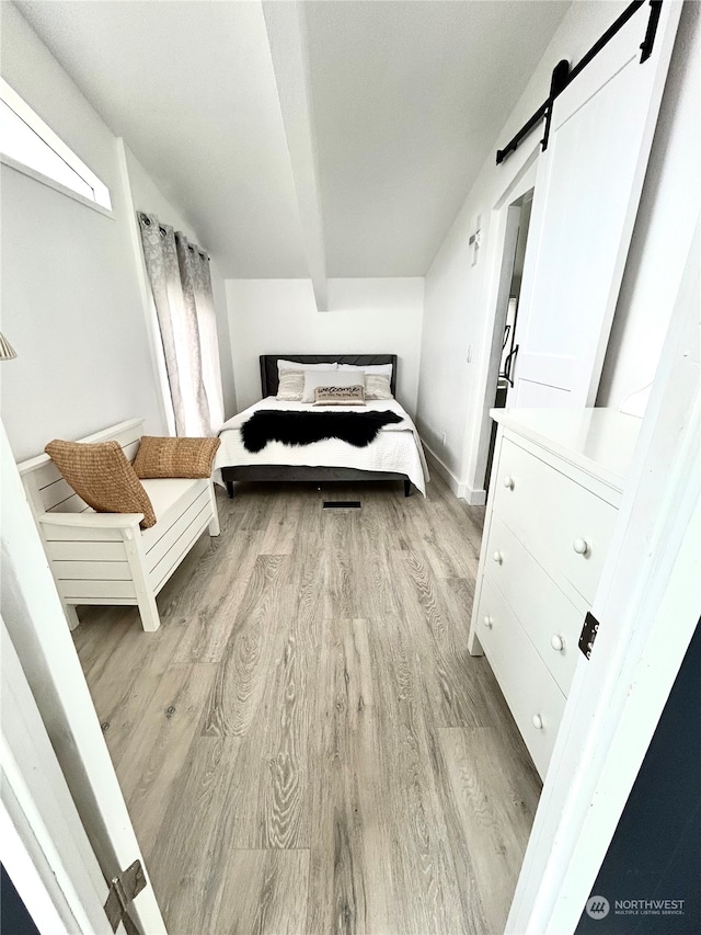 bedroom featuring a barn door, beamed ceiling, and light wood-type flooring