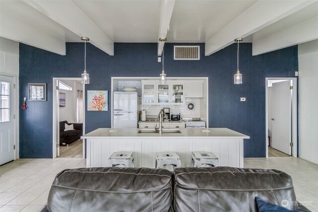 kitchen with a kitchen island with sink, beam ceiling, decorative light fixtures, white cabinets, and white fridge