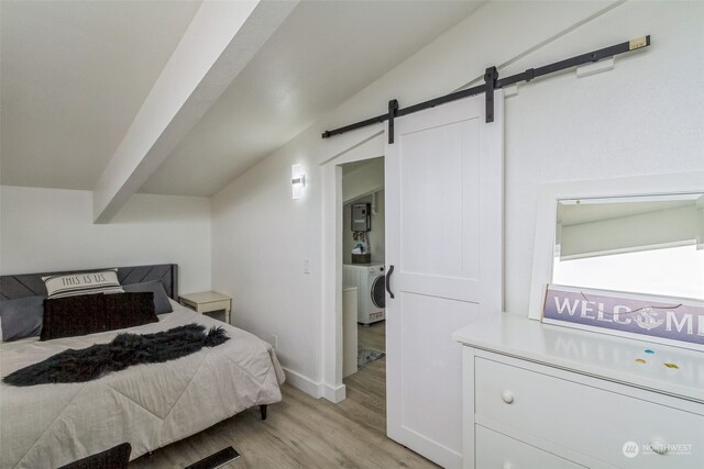 bedroom with a barn door, separate washer and dryer, light hardwood / wood-style floors, and lofted ceiling with beams