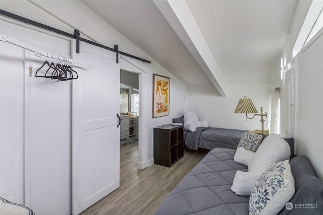 bedroom with a barn door, light hardwood / wood-style floors, and vaulted ceiling