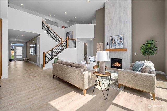 living room with a fireplace, light wood-type flooring, and a towering ceiling