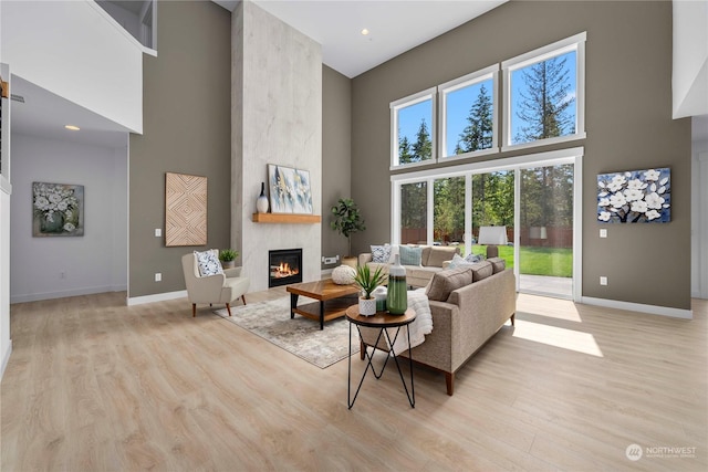 living room featuring a fireplace, light hardwood / wood-style floors, and a towering ceiling