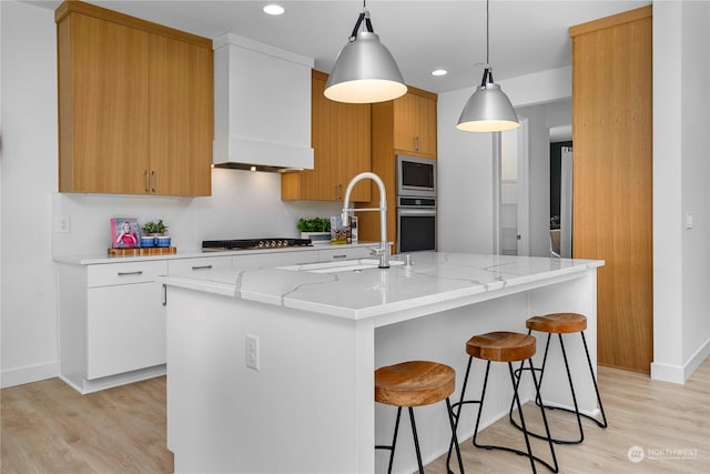 kitchen featuring a center island with sink, hanging light fixtures, light stone countertops, sink, and white cabinets