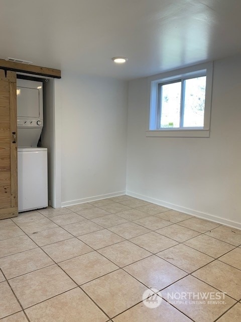 tiled spare room featuring a barn door and stacked washing maching and dryer