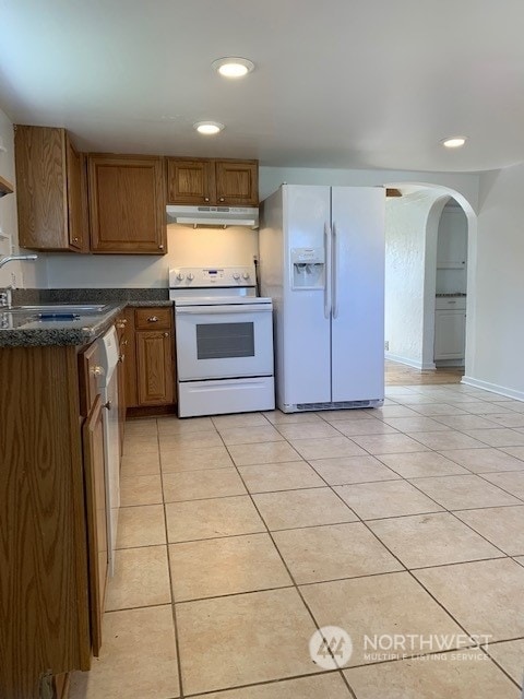 kitchen featuring white appliances, sink, light tile floors, and dark stone countertops