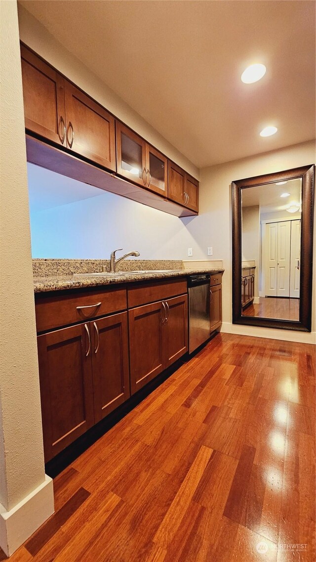 kitchen featuring light stone counters, sink, stainless steel dishwasher, and dark hardwood / wood-style floors