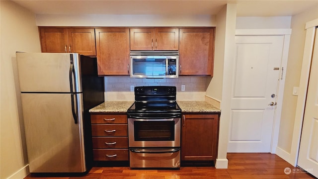 kitchen with dark hardwood / wood-style flooring, light stone countertops, appliances with stainless steel finishes, and tasteful backsplash