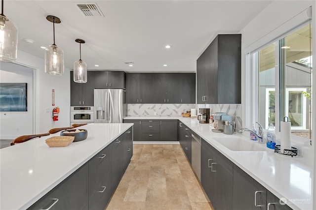 kitchen with pendant lighting, appliances with stainless steel finishes, sink, and backsplash