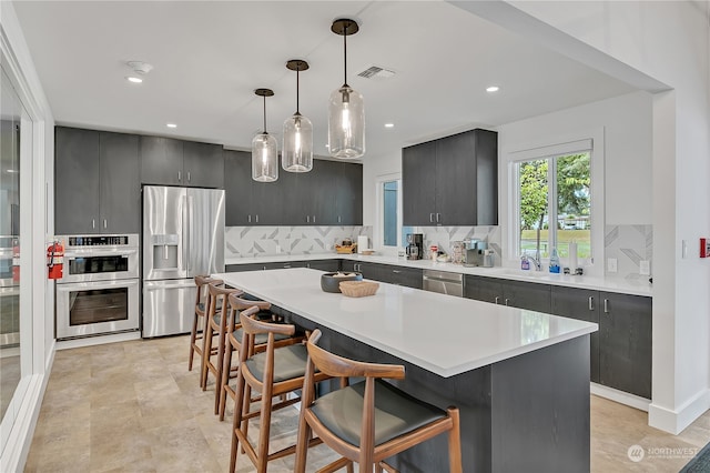 kitchen with hanging light fixtures, appliances with stainless steel finishes, a kitchen breakfast bar, a kitchen island, and decorative backsplash