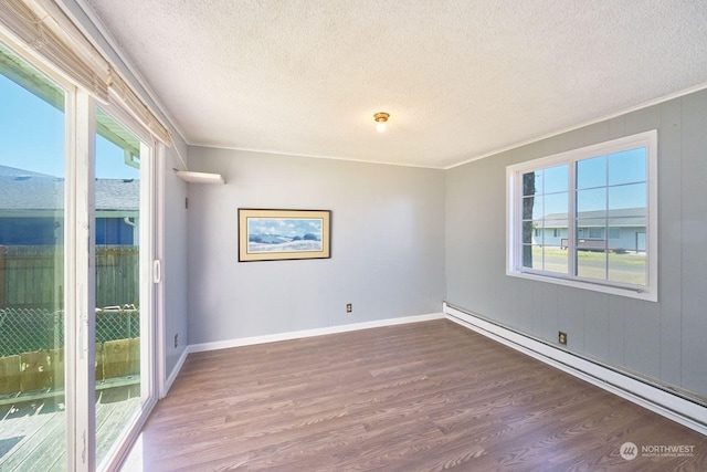 empty room featuring ornamental molding, dark wood-type flooring, a baseboard heating unit, and a textured ceiling