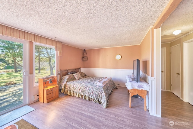 bedroom featuring a textured ceiling, access to outside, a baseboard radiator, and wood-type flooring