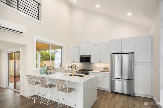 kitchen with high vaulted ceiling, sink, appliances with stainless steel finishes, a wall mounted AC, and white cabinetry