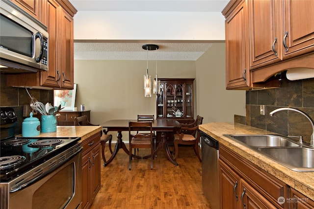 kitchen with appliances with stainless steel finishes, sink, dark hardwood / wood-style flooring, tasteful backsplash, and hanging light fixtures