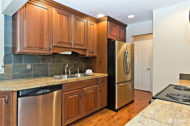 kitchen with appliances with stainless steel finishes, sink, backsplash, and light wood-type flooring