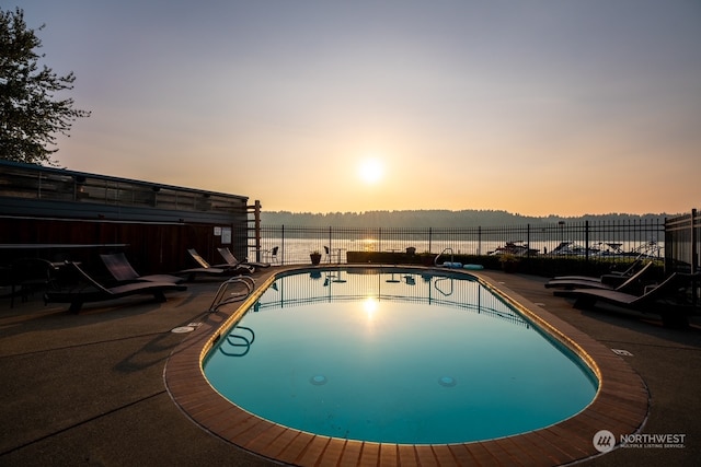 pool at dusk with a water view and a patio