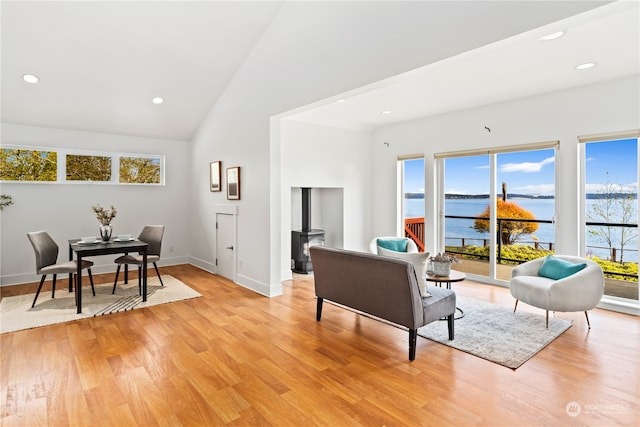 living room with plenty of natural light, light hardwood / wood-style floors, high vaulted ceiling, and a water view