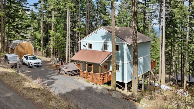 rustic home featuring metal roof, an outbuilding, gravel driveway, and a porch