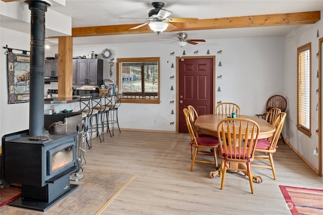 dining room with beamed ceiling, light hardwood / wood-style floors, ceiling fan, and a wood stove