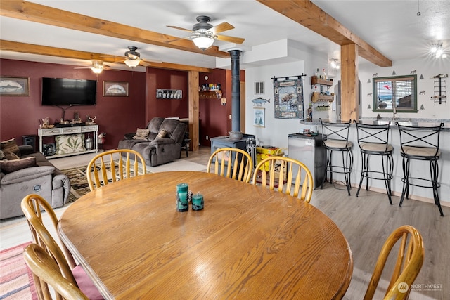 dining area with beamed ceiling, ceiling fan, a wood stove, and light hardwood / wood-style floors