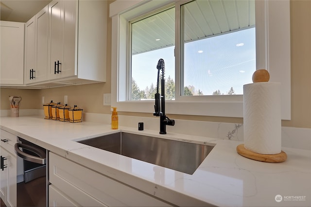 kitchen featuring dishwashing machine, white cabinets, sink, and light stone countertops