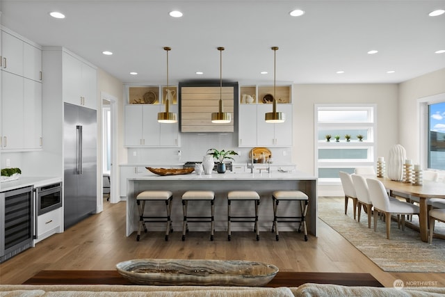 kitchen with hardwood / wood-style flooring, built in refrigerator, hanging light fixtures, and white cabinetry