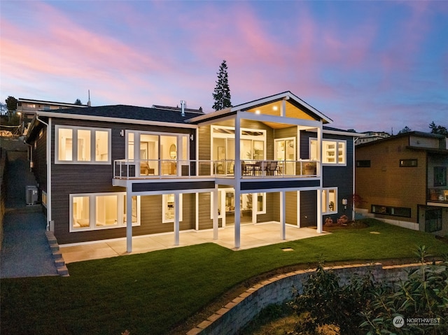 back house at dusk featuring a patio, a balcony, a lawn, and central air condition unit