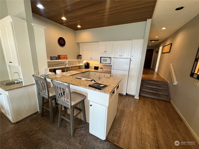 kitchen with light stone counters, sink, white appliances, white cabinetry, and kitchen peninsula