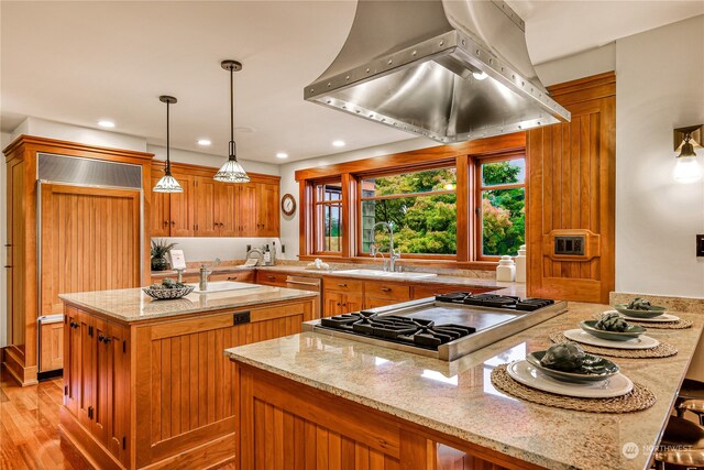 kitchen featuring paneled refrigerator, hanging light fixtures, island range hood, kitchen peninsula, and light hardwood / wood-style floors