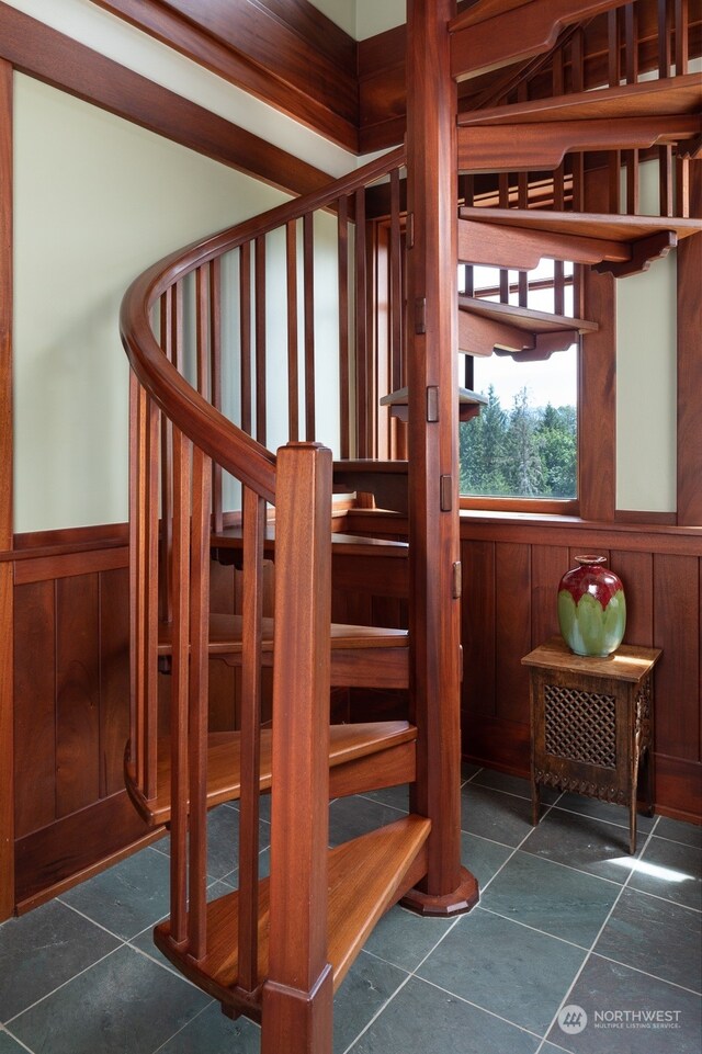 staircase featuring wood walls and dark tile floors