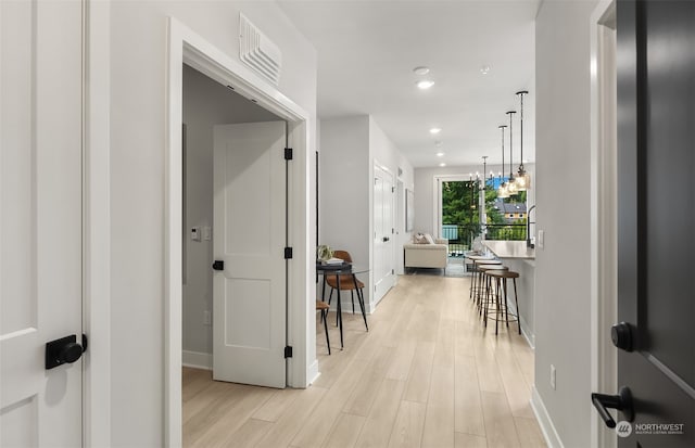 hallway with an inviting chandelier and light hardwood / wood-style floors